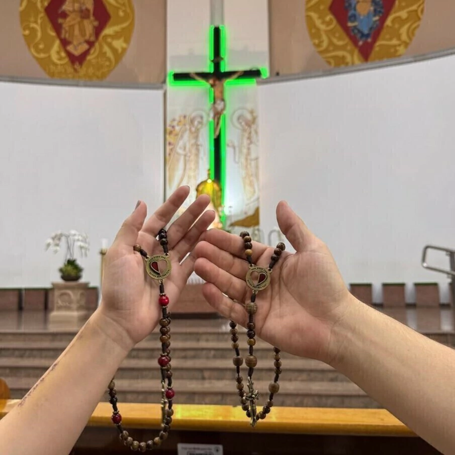 Duas mãos abertas com os terços diante do altar